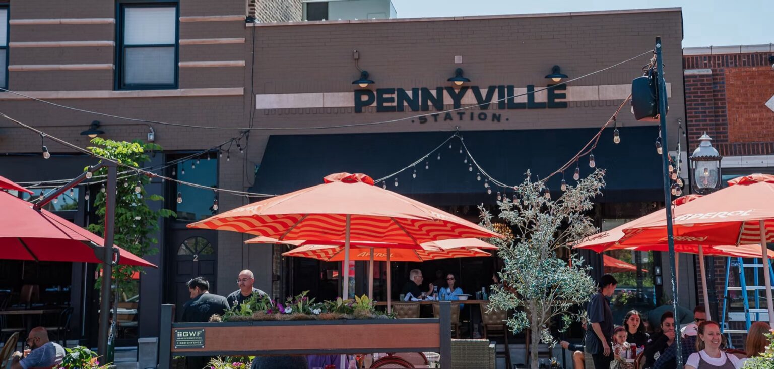 Pennyville Station restaurant patio in Park Ridge, Illinois, with outdoor dining under orange umbrellas.